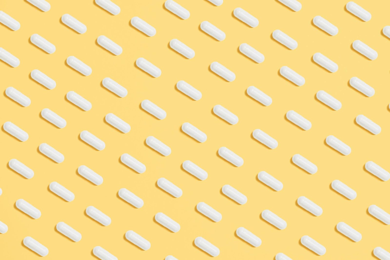 Pattern of white capsules on a bright yellow surface, symbolizing healthcare and medicine.