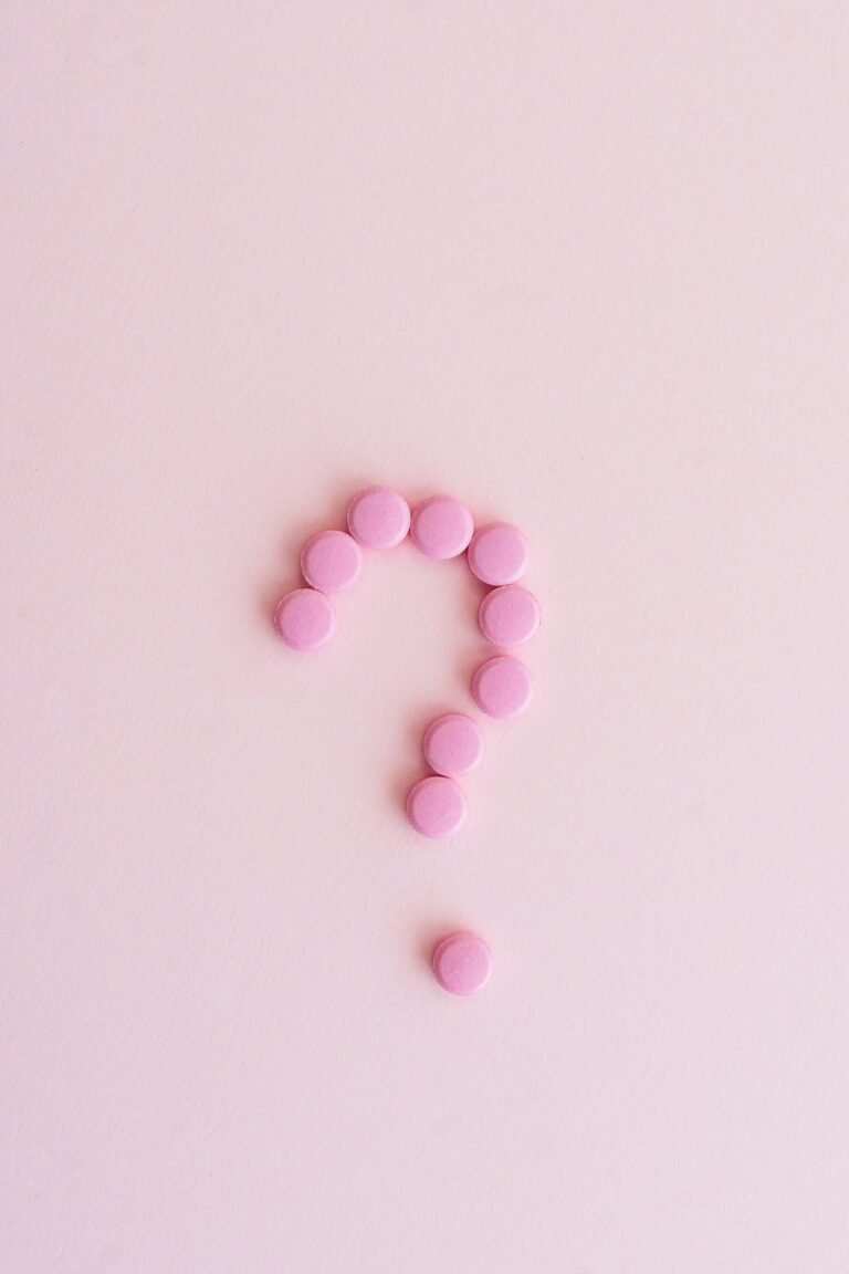 Pink pills forming a question mark on a pastel surface, symbolizing uncertainty in health decisions.