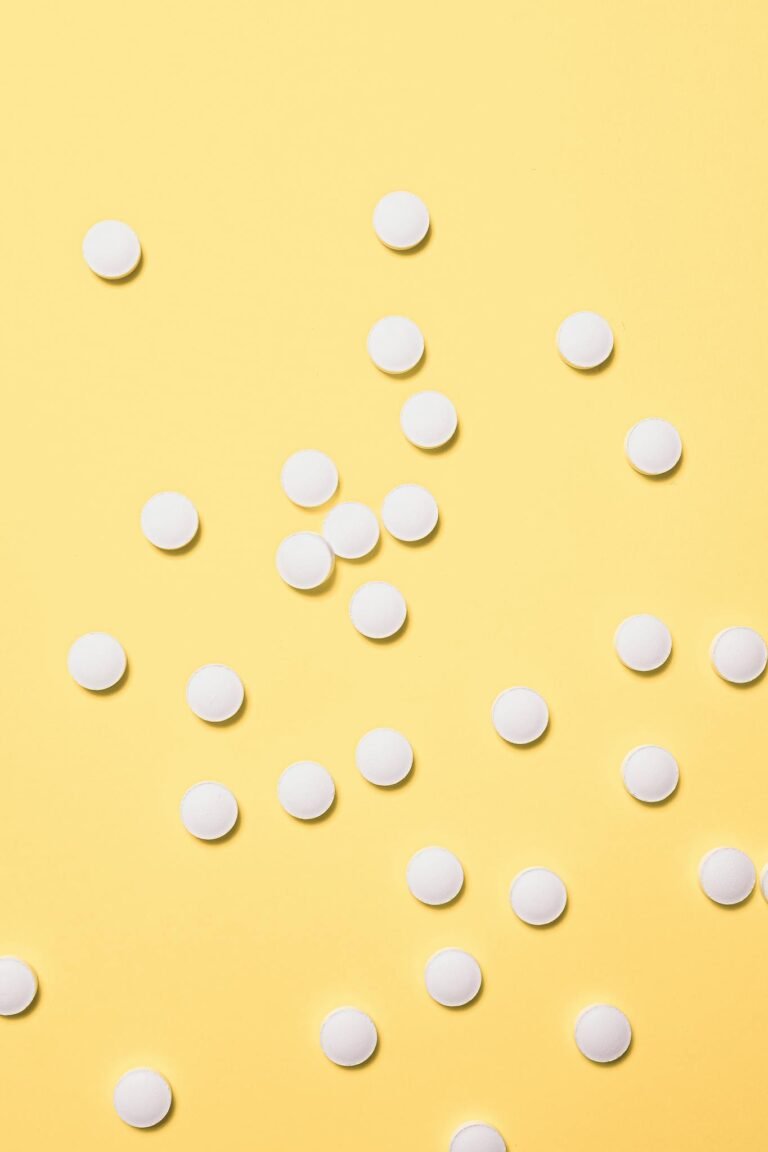 Scattered white pills on a bright yellow surface, ideal for medical themes.