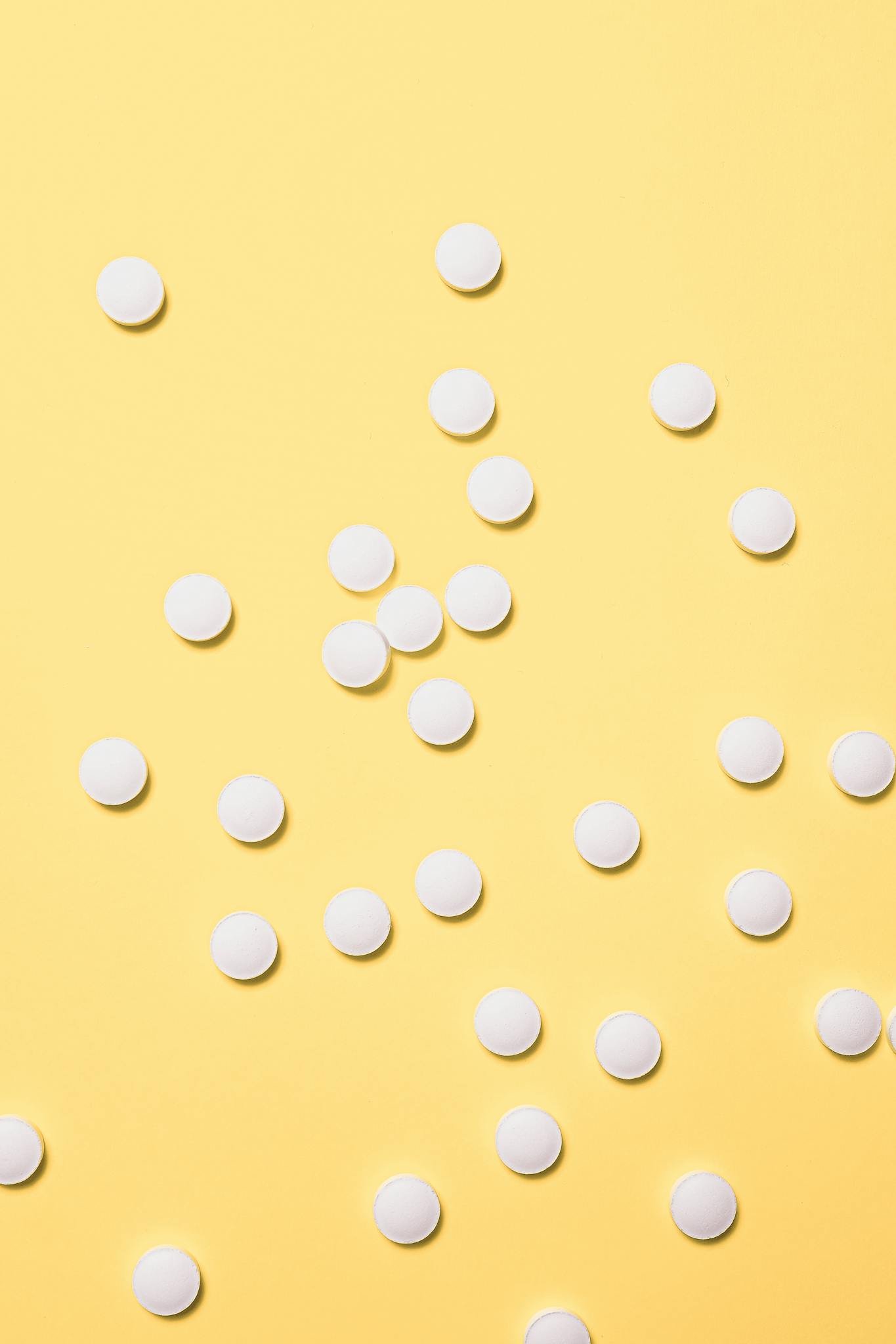 Scattered white pills on a bright yellow surface, ideal for medical themes.